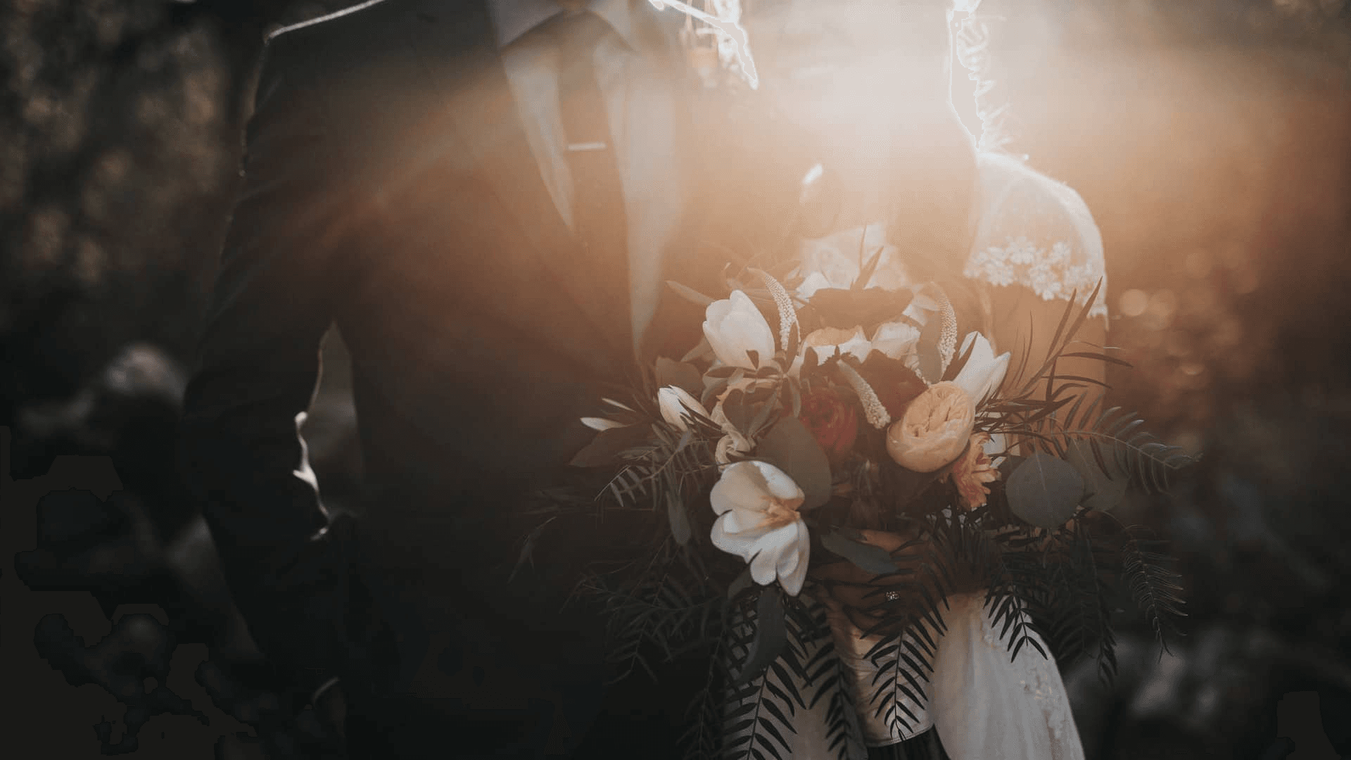 A couple stands together in a sunlit setting, holding a bouquet of flowers.