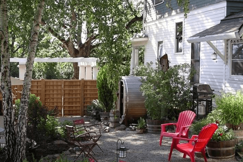 A cozy garden with red chairs, greenery, and a wooden hot tub beside a house.