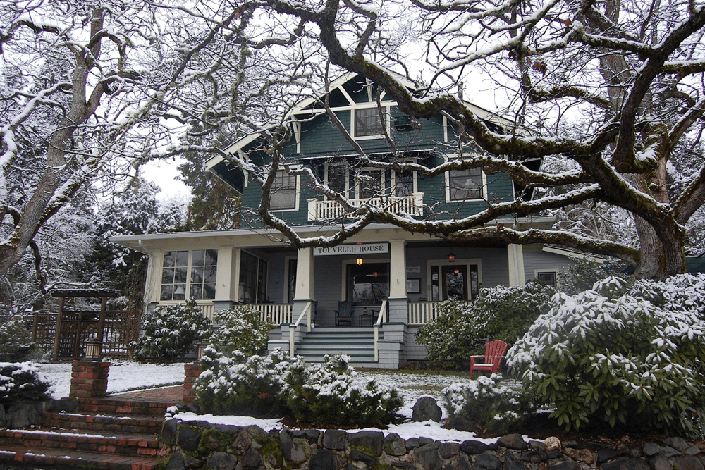 A large green house with snowy branches and a red chair in the front yard.
