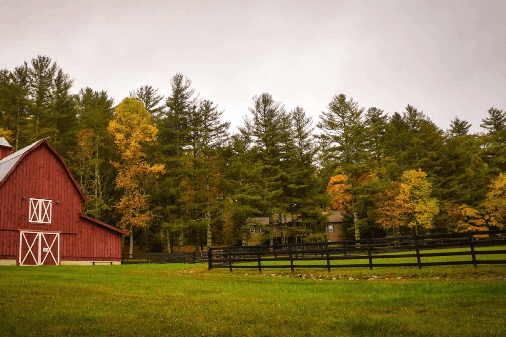A red barn surrounded by colorful autumn trees and a black fence.