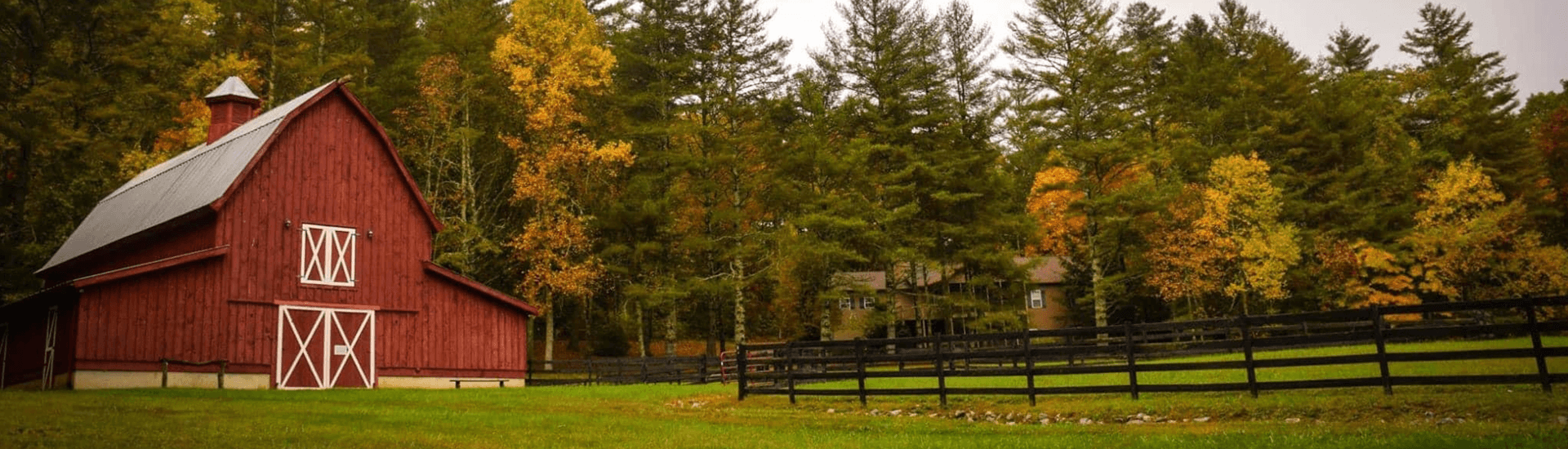 A red barn surrounded by autumn foliage and a black wooden fence.